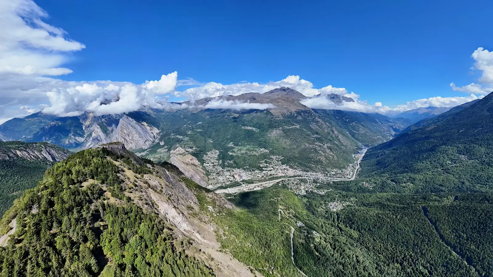 Panorama de la vallée de la Maurienne en été, entre crêtes boisées, sommets et villages au fond de la vallée de l'Arc